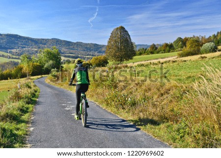 Woman riding a bike on  country road among meadows and hills in sunny autumn day, Low Beskids (Beskid Niski).
