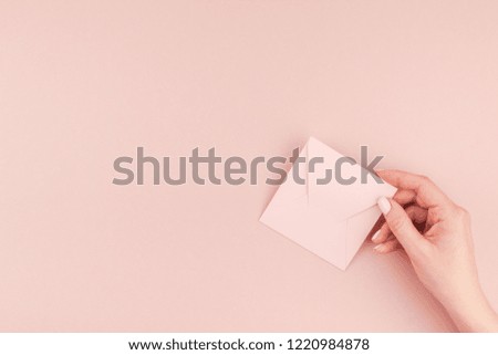Creative image of woman hand holding small love letter with copy space on millennial pink background in minimalism style. Concept template for feminine blog, social media