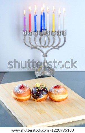 Image of jewish holiday Hanukkah background with menorah traditional candelabra  also called a Hanukiyah,  jelly or jam doughnut sufganiyot, chocolate sufganiyah and burning candles.
