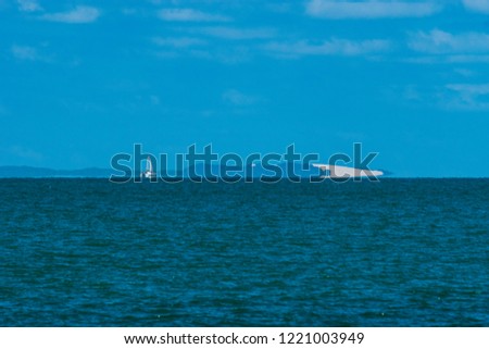 a distance photo of Moreton Island's southern end with a calm bay blue afternoon sky and a catamaran sailing along the horizon