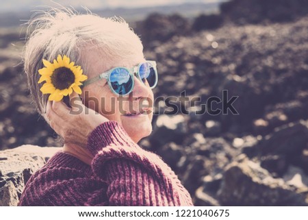 Beautiful adult old woman with yellow sun flower on his head take the sun and enjoy the lifestyle in outdoor natural place. Smile and happiness for mature female with defocused bokeh background