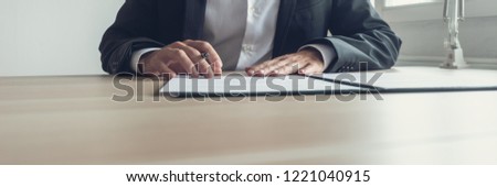 Wide view image of businessman sitting at his office desk with pen in one hand reading a document in an open binder. With retro vintage effect.
