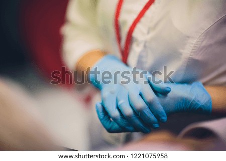 Close up of female doctor's hands putting on blue sterilized surgical gloves in the office.