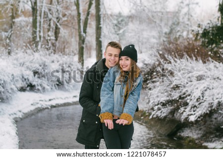 A stylishly dressed lovers couple in the snowy snowy park near water