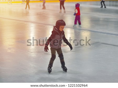 Adorable little boy in winter clothes with protections skating on ice rink
