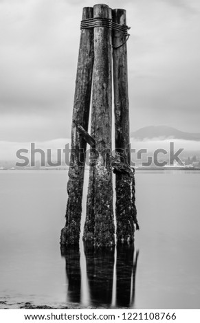 Large supports from long gone structures sit in a pacific northwest bay. Long exposure smooths the water and sky to a misty bliss