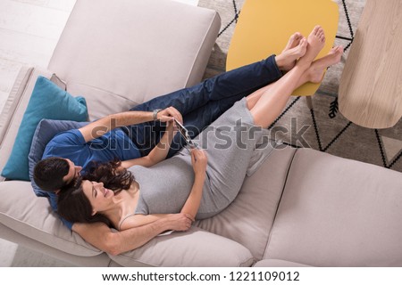 top view of a young pregnant couple looking baby's ultrasound photo while relaxing on sofa at home
