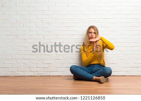 Young girl sitting on the floor making stop gesture with her hand to stop an act