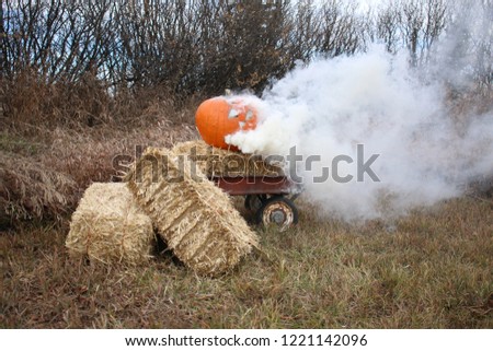 A bright orange pumpkin has been cared into a Hallowe'en Jack-o-lantern and filled with smoke while sitting on a yellow straw bale in an old rusty wagon.
