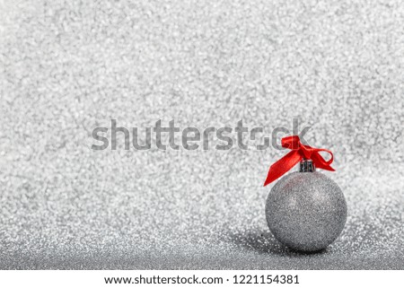 Christmas holiday composition of festive decor ball with red ribbon bow on silver glitter bokeh background