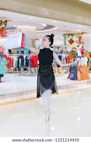 Picture of a young woman holding paper bags while dancing with tiptoe poses in the mall