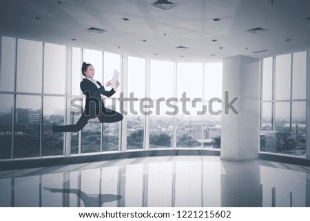 Picture of beautiful ballerina wearing suit while using with a digital tablet and jumping in the office