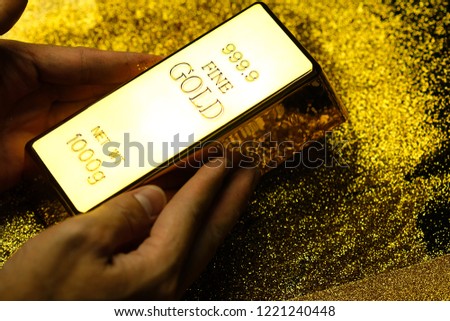 Gold bar in hand of man on a gold glittering background, The concept of gold is precious.