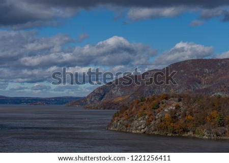 Fall landscape. Daylight; river, hills, trees with colorful foliage. Blue sky with clouds. 
