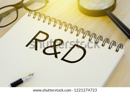 Business and finance conceptual. Sunglasses,pen,magnifying glass and notebook written with R&D (Research and Developement) on wooden background.