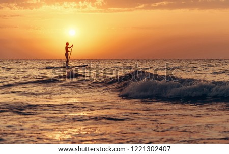 Silhouette of young man paddling on a SUP board in the sea at sunset.