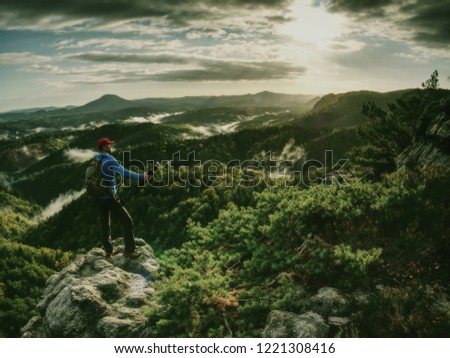 Freelancer create nature photos. Professional photographer takes photos with camera on tripod on rocky peak. Dreamy fogy landscape