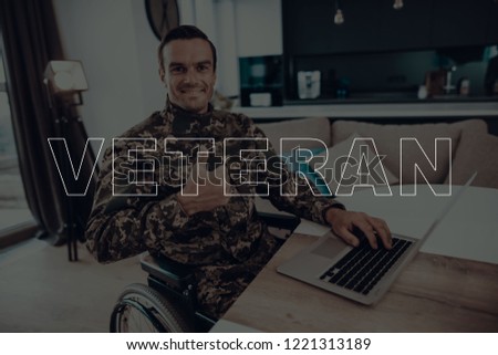 Military Veteran. Disabled in a Wheelchair. Man Sitting at Table.Using s Laptop. Man is Soldier. Soldier in Military Uniform.Showing OK Sign. Man Smiling. Man Located in the Living Room.