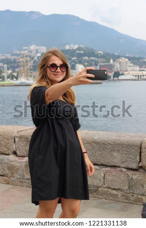 Beautiful blonde girl in a black spectacular dress on the background of the resort city of Yalta makes selfi or is broadcast. Russia, Crimea