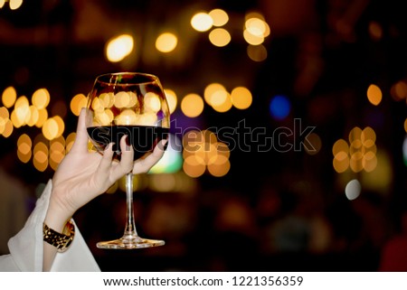 Red Wine Party.  Elegant Young Woman Having a Glass of Red Wine Against Blurred Bokeh Nightclub. Picture Presenting Happy Beautiful Girl with Red Wine