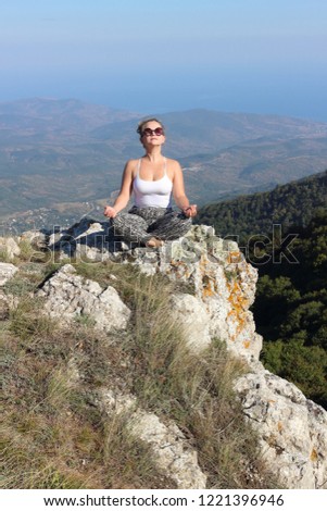 A burning blonde on the top of a mountain plateau in the Crimea is meditating in the lotus position. Active and slim girl happy in freedom, traveling along the Black Sea coast