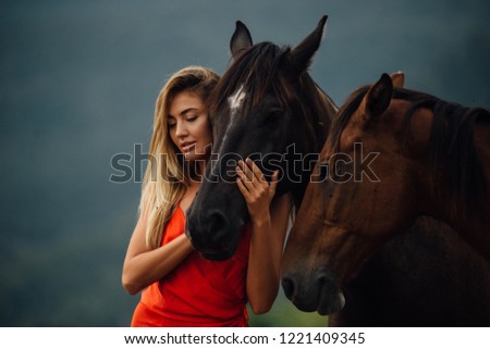 Close-up portrait of blonde woman with chestnut horses. Girl in the red dress holding horse head. Tender and care picture. 