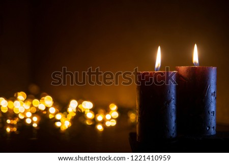 Two candles on black background with blurred Christmas lights