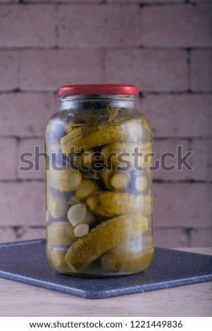 jar of pickled cucumbers on a cutting board on a brick wall background