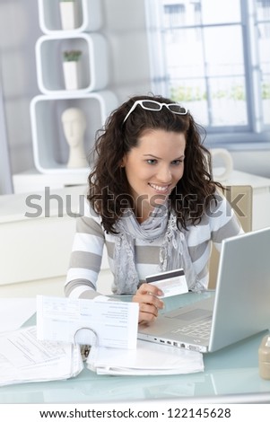 Happy woman shopping online, holding credit card, using laptop computer, electronic purchase.