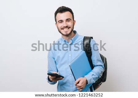 Portrait of cheerful handsome man holding laptop and phone over white background and looking at the camera. Royalty-Free Stock Photo #1221463252