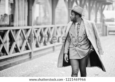Stylish African American man model in gray coat, jacket tie and red hat posed at foggy weather street. Black and white photo.