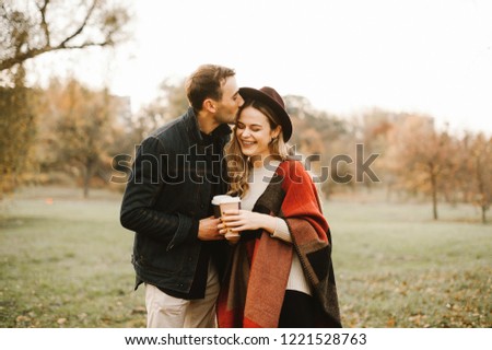 Young couple in love hugging, having fun and smiling in the park on a sunny autumn day and drinking tea