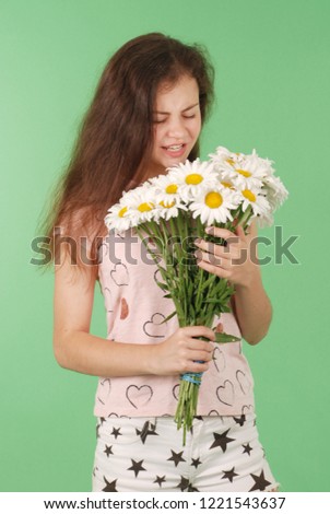 Studio portrait of allergic brunette young gir, having an allergic reaction to flowers - chamomile, selective focus. Isolated on green background