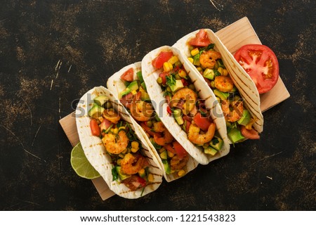 Shrimps tacos with salsa, vegetables and avocado on a dark background. Mexican food.Top view