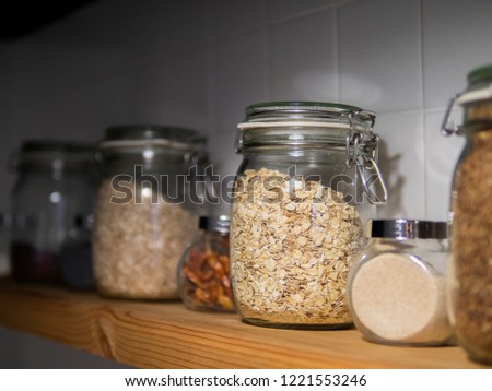 Various uncooked cereals, grains, beans and pasta for healthy cooking in glass jars on wooden table, white background, close-up. Clean eating, vegan, balanced dieting food concept
