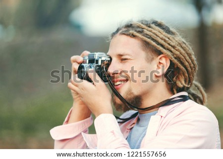 Hipster blonde bearded photograph boy with dreads smiling while taking pictures on the nature location in the forest, outdoor view