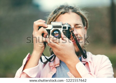 Hipster blonde bearded photograph boy with dreads taking pictures on the nature location in the forest, outdoor view