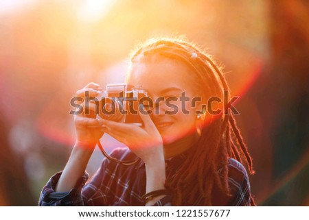 Portrait of hipster cute girl with dreads holding camera and taking pictures in the sunset in the forest, outdoor view