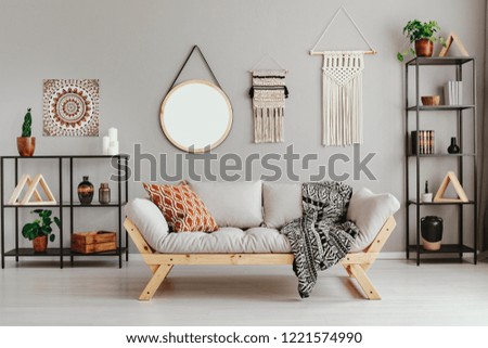 Macrame, mirror and ethno graphic on beige wall in stylish living room interior with metal furniture and comfortable couch and patterned pillow and blanket Royalty-Free Stock Photo #1221574990