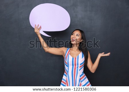 Image of excited asian woman 30s holding blank thought bubble above her head with copyspace for your text standing isolated over gray background