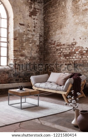 Wooden table on carpet in front of settee in loft interior with flowers and red brick wall. Real photo
