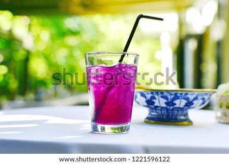 Gladd iced bluepea juice with lemon, syrup with straw, blured side blueand white dish of snack on white cloth table blurred green bokeh of garden background, beautiful color drink in cute party  