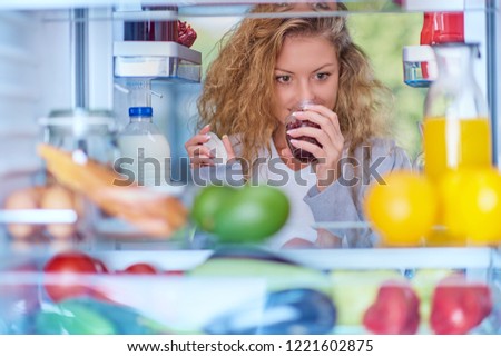 Woman smelling jam in front of fridge full of groceries. Picture taken from the iside of fridge.
