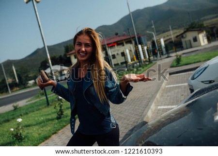 Smiling beautiful woman in jeans jacket standing on the parking next to the car. Travel by automobile around the Armenia. 