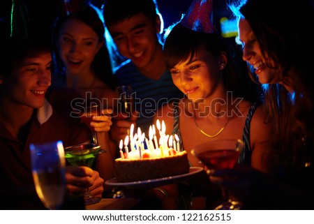 Portrait of joyful girl looking at birthday cake surrounded by friends at party