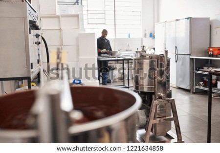Worker in an artisanal chocolate making factory preparing ingredients with melted chocolate being turned in a stainless steel mixer