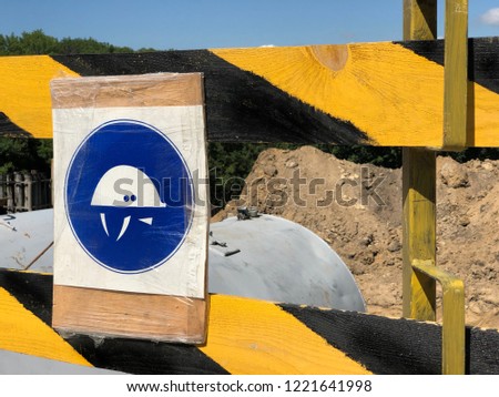 close up of helmet sign attached on the yellow and black wooden fence. a sign is warning to put a helmet on the construction site because of danger

