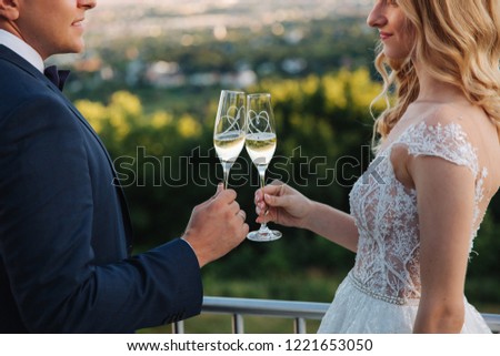 Groom and bride stand on the background of the city and drink champagne from wineglass. Clink glasses