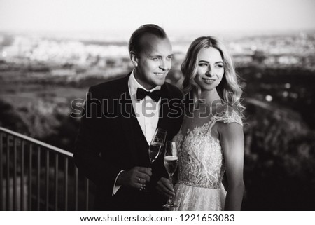 Wedding couple stand on the background of the city and drink champagne from wineglass. Black and white picture
