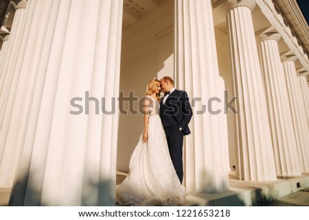 Man and woman in wedding clother stand near the big pillar